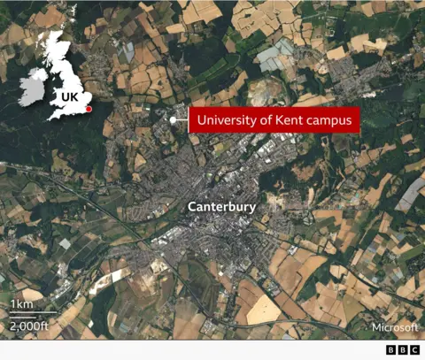A satellite image of Canterbury and the surrounding area. A labels shows that the campus of the University of Kent is on the outskirts of the city about three kilometres (two miles) north of the city centre. Suburbs connect the campus to the city but to the north is mainly farmland and woods