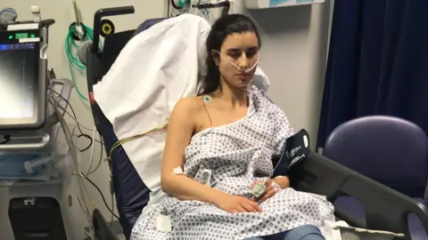 Harriet Davidson Harriet Davidson wearing a hospital gown in a hospital bed. She has her right upper chest and arm exposed and is hooked up to various pieces of medical equipment.