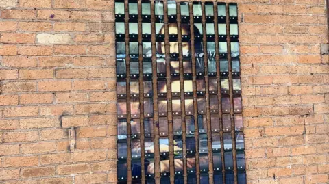 One hundred iPhones are pinned onto a brick wall and each screen shows a snippet of the Mona Lisa portrait
