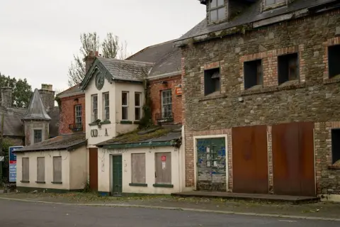 A run-down, erstwhile  handsome gathering  with a achromatic  facade, boarded up   windows and breached  signage - the remaining letters work   "..OLD...A.." 