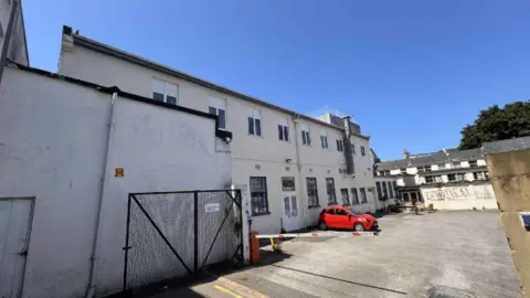 A large white building around a courtyard with one red car parked outside