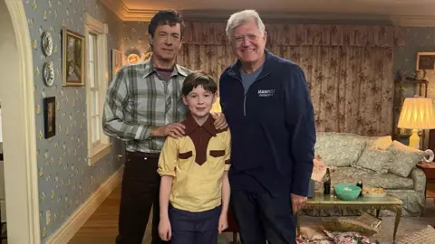 (l-r) Actors Tom Hanks, Albie Salter and director Robert Zemeckis on set.
Tom is dressed in jeans and a checkered shirt, whilst Albie is wearing jeans and a yellow top and Robert is wearing a navy tracksuit.