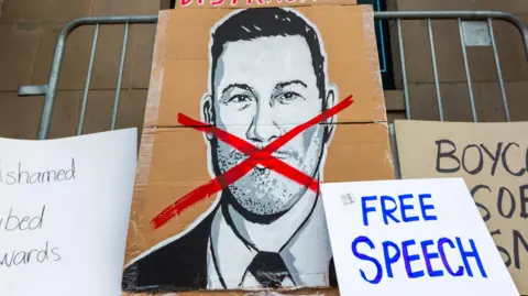 Getty Images A large cardboard placard with an illustration of Jimmy Kimmel and a red cross across his face, alongside other signs including one reading 