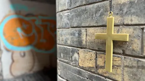 A cross hangs next to an alley in Glasgow city centre where people frequently use illegal drugs