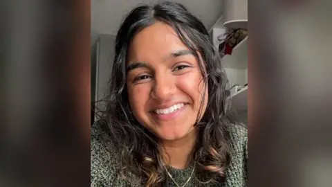 Family handout A woman with mid length dark hair, wearing a green woollen jumper is smiling at the camera. She is wearing a gold necklace.