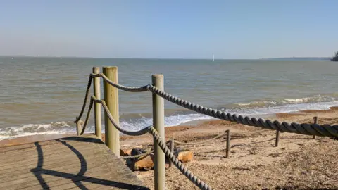 Sunseeker A wooden platform with rope barriers on a sandy beach, the sea beyond.