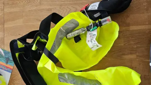 Salcombe RNLI A picture of a lifejacket used by one of the sailors involved in the Salcombe incident. The lifejacket is yellow hi-vis and there is a cylinder with a red tag at the top.