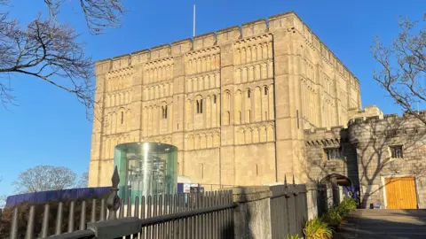 Shaun Whitmore/BBC The exterior of Norwich Castle. It is a square Norman keep made of pale brown stone. A path with railings leads to a smaller part of the castle next to the keep. 