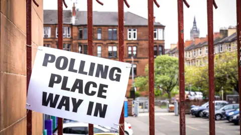 PA Media A polling place sign with black text on white paper attached to slightly rusted orange railings in Glasgow