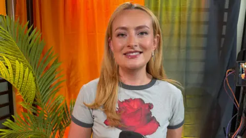 Amelia Dimoldenberg wearing a T-shirt in a studio with orange curtains