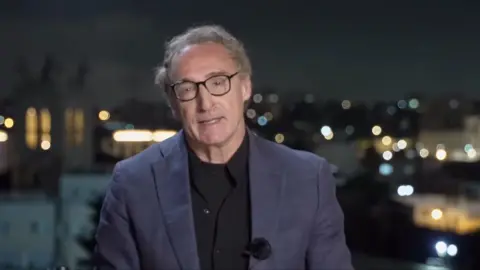 A BBC journalist speaks to camera during the night in the Middle East.