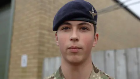 Cadet Cpl Drew Bryson, who has dark hair and is wearing his military uniform of camouflaged clothing and a dark blue beret.