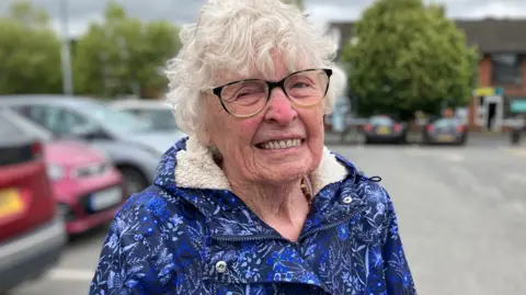 BBC A pensioner in a blue jacket and rimmed glasses smiles for the camera