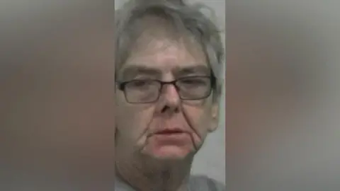 Northumbria Police Mugshot of Maria Chambers. She is an older looking lady with messy grey hair and black glasses. Her eyes are half closed.