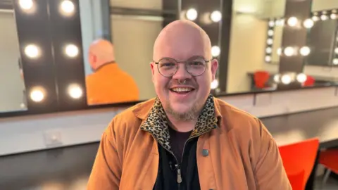 Adam Carver posing in the dressing room of the Birmingham Rep with lights behind them