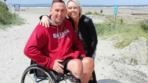 Shaun Gash in a wheelchair on a beach with his wife