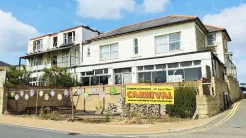 The Tarvic 2 Hotel is raised from the street. It is made up of two white structures, one two floors and on three floors. Both buildings look run-down.