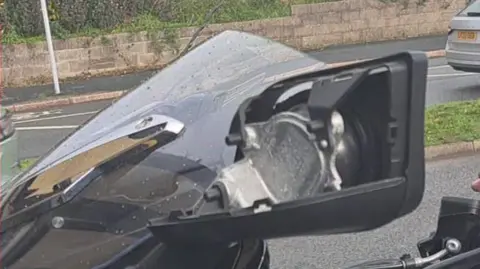 Peter Horgan An upper section of a black motorcycle. Beside the windscreen is what appears to be a mirror housing with the back of it missing. 