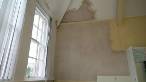 A large white wall which has recently been plastered, with a large white window next to it