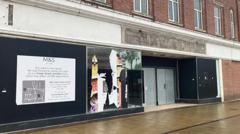 A brick-built, two-storey building with blacked-out windows and doors. There are posters and damage to some parts of the black cladding.