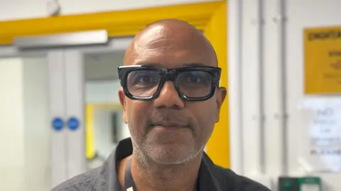 George King/BBC A head and shoulders image of a man wearing black glasses. He is smiling and looking into the camera. 