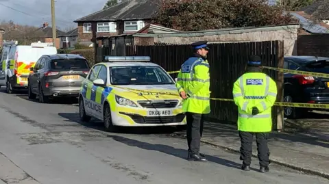 Two community support officers in yellow high-vis coats on guard near a residential garage