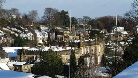 In the distance is a stone building with turrets, large windows and snow on nearby roof tops