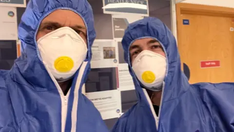Correspondent Alastair Fee left and Cameraman Brandon Walsh right both in blue overalls with protective face masks.
