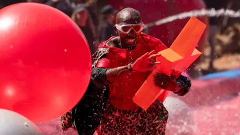 Sir Mo Farah splashes through red water carrying a large red star