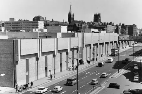 Picture Nottingham The Broad Marsh shopping centre in 1975 shows a black and white photograph of a concrete building with cars driving in the street next to it.