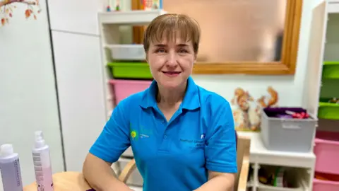 Becki Bowden / BBC A person in a blue polo shirt with the Northern Lincolnshire and Goole NHS Trust logo sits at a table. There are coloured boxes in the background.