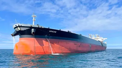 A large tanker, painted orange and black, sailing through blue sea waters on a clear day