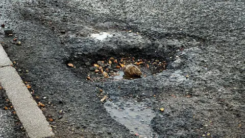 Getty Images A pothole in the road surface with a few small pebbles and some standing water