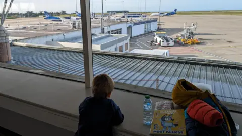 A child can be seen from behind watching planes from the observation deck above the runway at Jersey airport. 