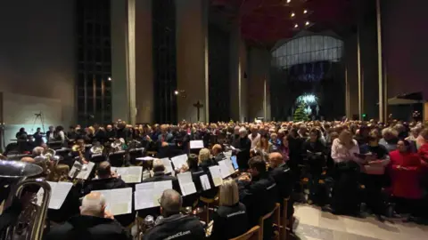 A brass band playing inside a cathedral in front of a large audience