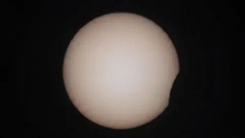 The start of the solar eclipse in Braunton, Devon. The shadow of the moon can be seen starting to cover the edge of the sun in the bottom right. The Sun is seen as a white circle on a black background.