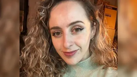 Marianne Ward wearing a light green jumper, she has curly hair and is smiling.