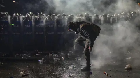 Anadolu via Getty Images A demonstrator wearing a gas mask stands in front of a line of riot police during a protest