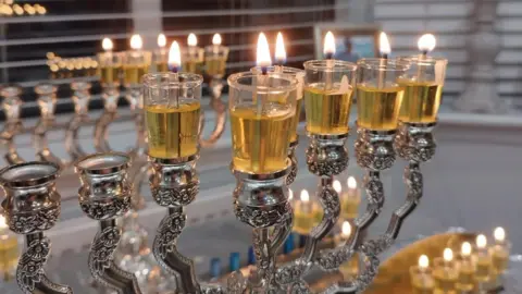 A hanukkiah whose sticks are filled with oil. It is a an ornamental candle stick made from silver with nine branches, each holding a small candle in a glass jar