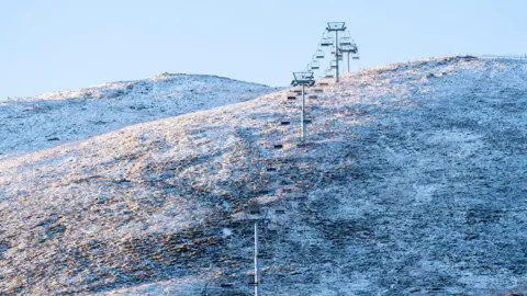 PA Media A hill covered in a light cover of snow with a cold white sky. A ski lift can be seen in the distance on the hill.