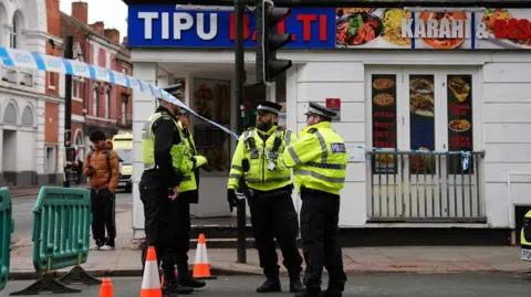 PA Media Four police officers in fluorescent jackets standing outside a kebab shop and police tape