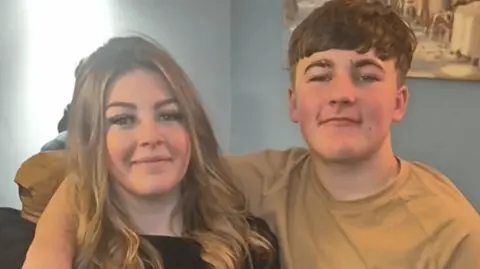 The picture shows two people smiling at the camera. Cherish Bean on the left has brown, long hair, and Ethan Slater on the right has short brown hair. 