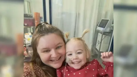 NHS Blood & Transplant Selfie of mum Jodie and Amelia in a hospital room. Both have big smiles on their faces.