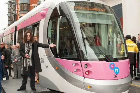 Getty Images Ozzy Osbourne stands beside a pink, silver and white tram bearing his name