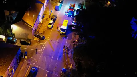JMG Press Drone shot from above of the street with the car hitting the house and emergency vehicles and a cordon