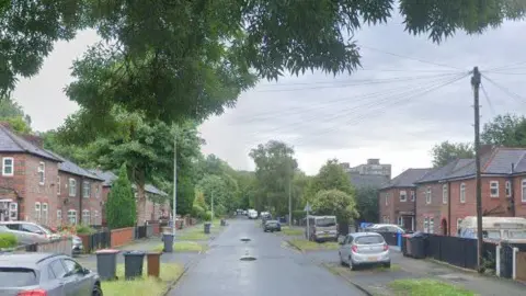 Google A view of South Radford Street with red brick semi-detached houses on the left and right with cars parked on the grass and pavements. 