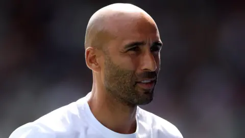 Lee Grant, wearing a white t-shirt, looks on