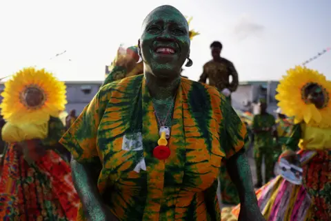 Reuters A woman smiles, wearing a green and orange tie-dye outfit. She is covered in green glitter.