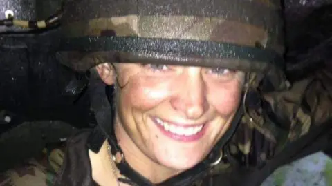 Handout Woman smiling at the camera in a camo military hat and a camo jacket. 