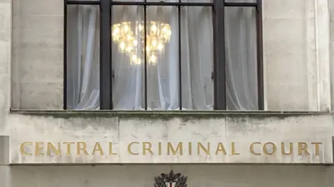 The front of the Old Bailey with the words Central Criminal Court in gold and  illuminated lamps showing though the window.